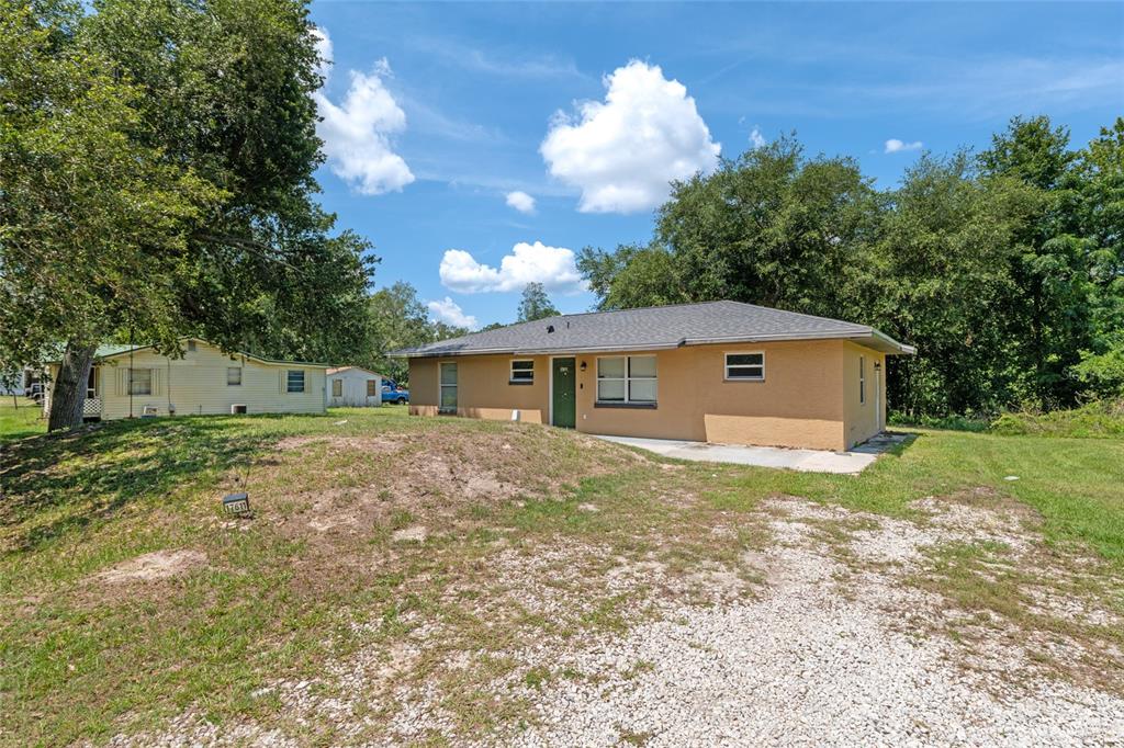 A tan, single-story house with a dark green door sits on a gravel lot — 17611 FL33, GROVELAND, FL