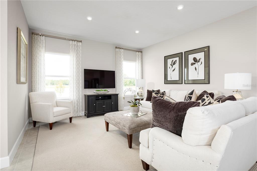 A bright living room features white sofas, a patterned ottoman, and a wall-mounted television — 11149 NELLIE CROSSING CIRCLE, CLERMONT, FL