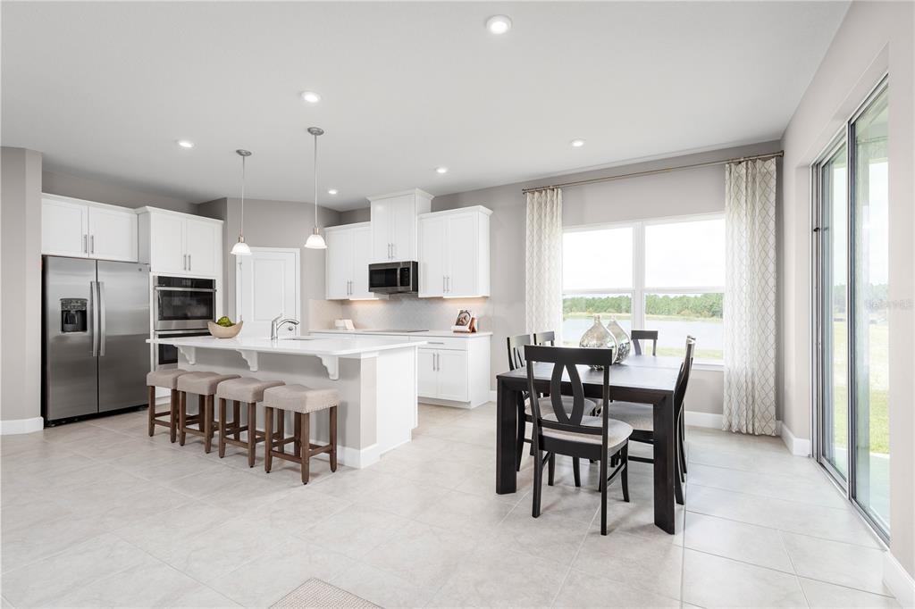 A modern kitchen features white cabinets, stainless steel appliances, a center island, and dining area — 11149 NELLIE CROSSING CIRCLE, CLERMONT, FL