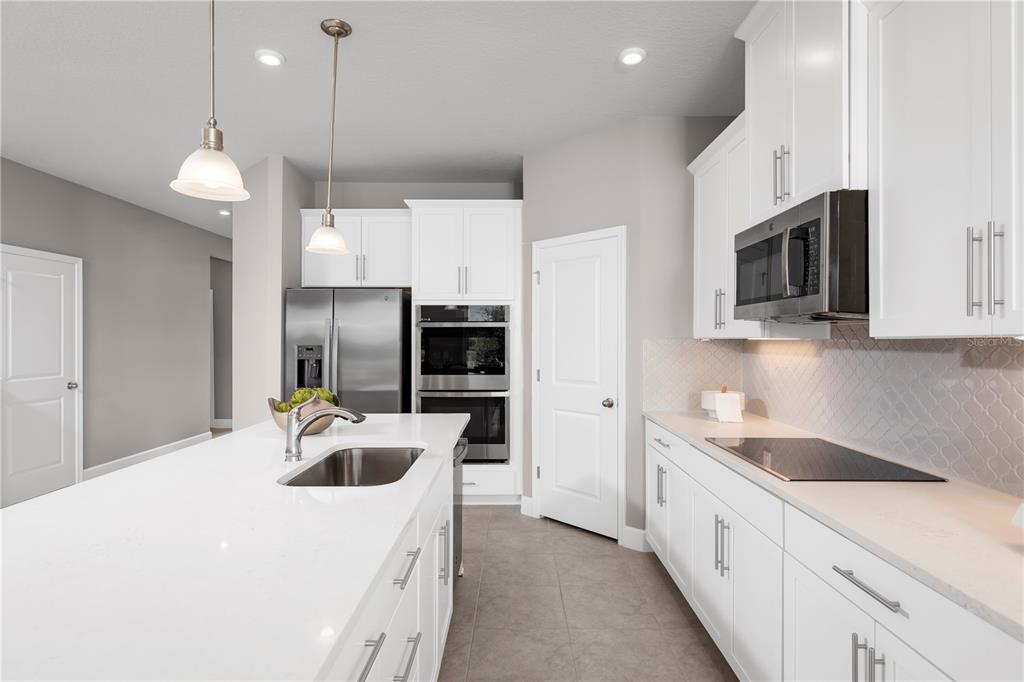 A modern kitchen features white cabinets, stainless steel appliances, a large island, and tile flooring — 11149 NELLIE CROSSING CIRCLE, CLERMONT, FL