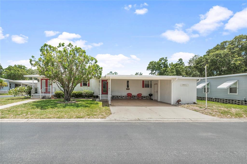 A single-story manufactured home features a white exterior, a carport, and a large front tree — 12501 ULMERTON ROAD UNIT 217, LARGO, FL