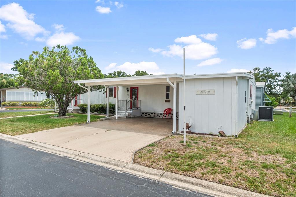 A single-story mobile home features a white exterior, a concrete carport, and a red front door — 12501 ULMERTON ROAD UNIT 217, LARGO, FL