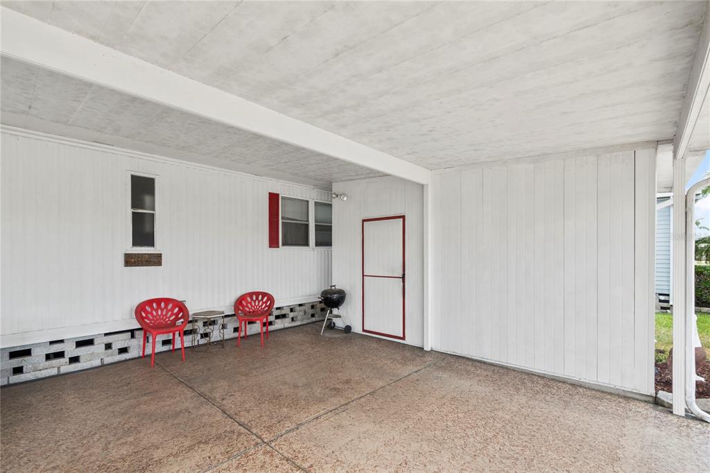 A covered concrete patio features white siding, two red chairs, and a small charcoal grill — 12501 ULMERTON ROAD UNIT 217, LARGO, FL