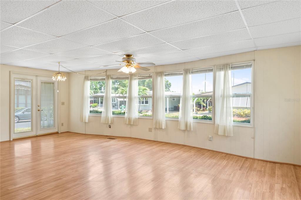 A sunroom with light wood flooring, a drop ceiling, and large windows with white curtains — 12501 ULMERTON ROAD UNIT 217, LARGO, FL