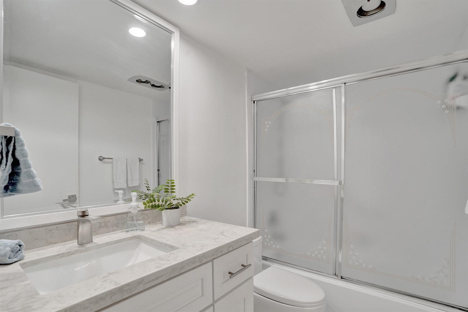 A bathroom features a white vanity with a marble countertop, mirror, and a glass-enclosed shower — 1211 Bahama Bend # E1, Coconut Creek FL 33066, COCONUT CREEK, FL