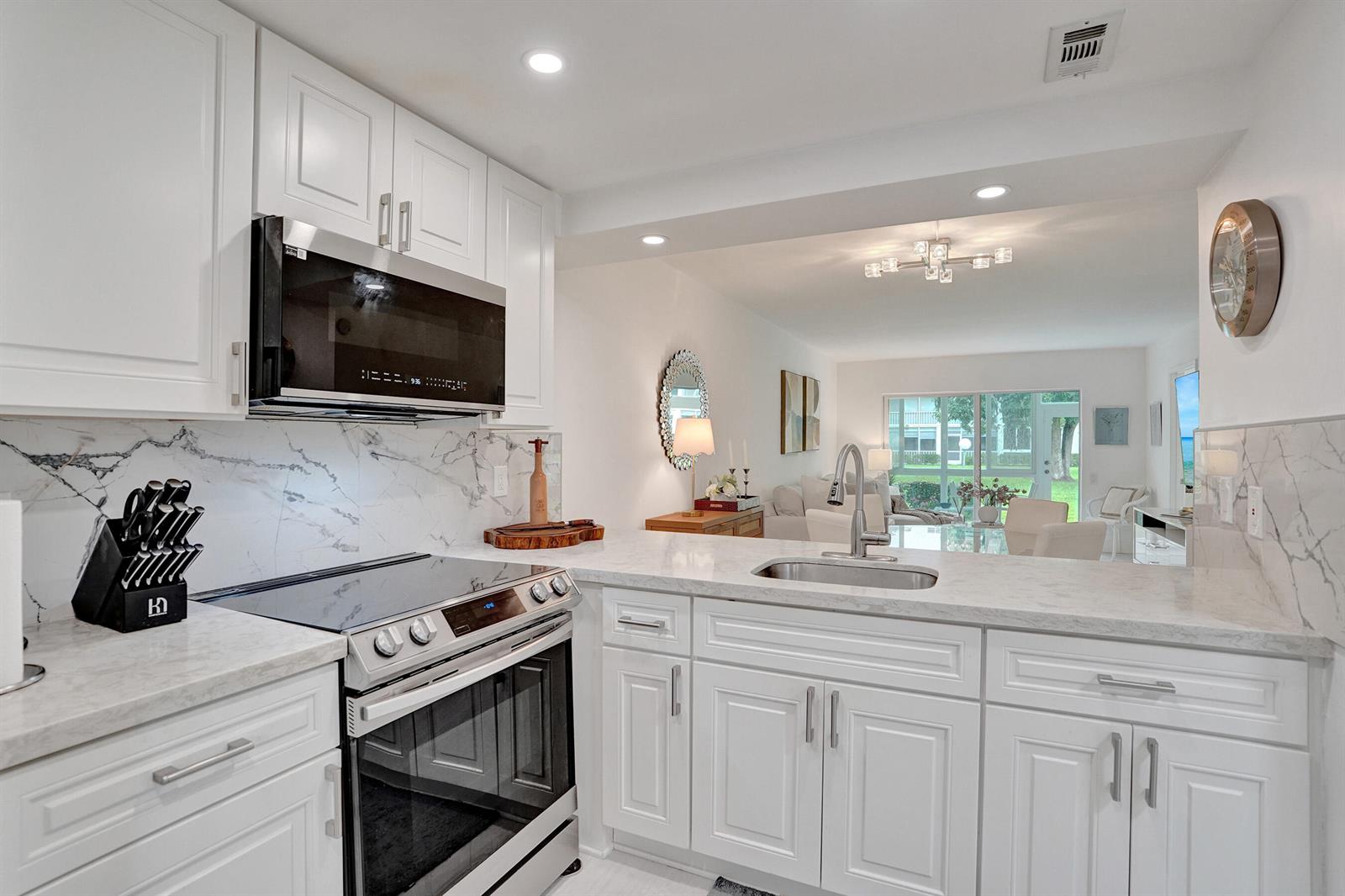 A white kitchen features marble countertops, stainless steel appliances, and an open view to the living area — 1211 Bahama Bend # E1, Coconut Creek FL 33066, COCONUT CREEK, FL