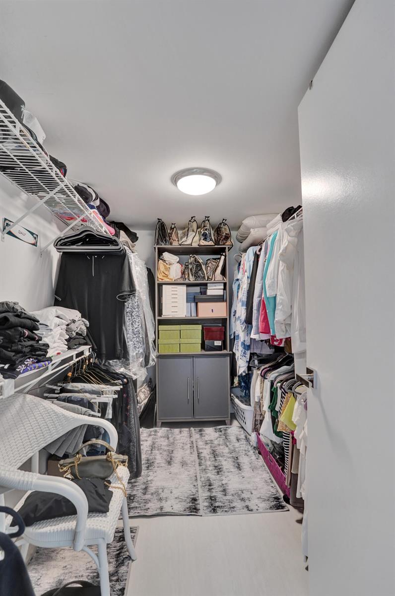 A walk-in closet features white wire shelving, a central storage cabinet, and hanging clothes — 1211 Bahama Bend # E1, Coconut Creek FL 33066, COCONUT CREEK, FL