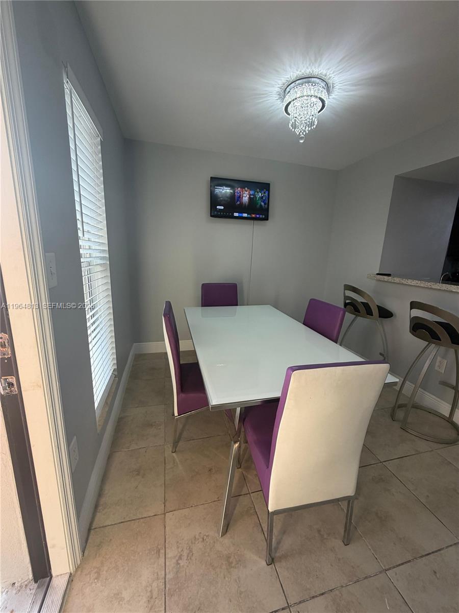 A dining area features a white table, purple chairs, a crystal chandelier, and a wall-mounted television — 1955 NW 5th Pl # 13, Miami FL 33136, MIAMI, FL