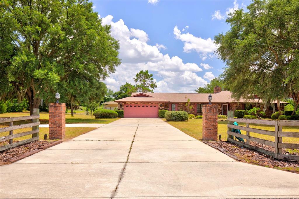 A long concrete driveway leads to a single-story brick house with a pink garage door — 4711 COUNTY ROAD 134, WILDWOOD, FL