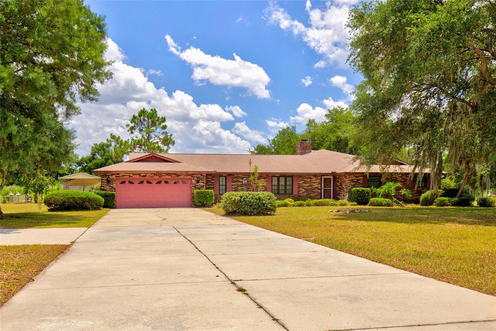 A single-story brick house with a pink garage door sits at the end of a driveway — 4711 COUNTY ROAD 134, WILDWOOD, FL