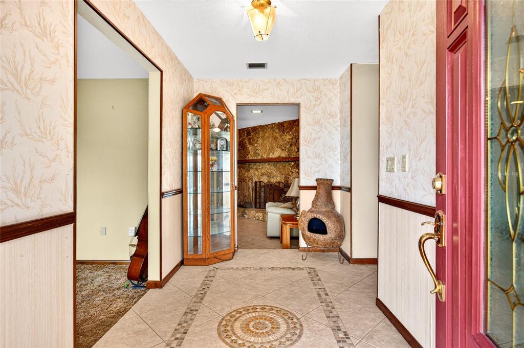 An entryway features tiled floors with a central medallion, wallpaper, and a glass display cabinet — 4711 COUNTY ROAD 134, WILDWOOD, FL
