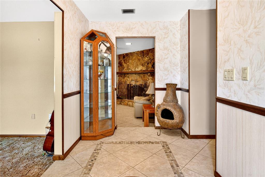 A tiled entryway features a glass display cabinet, a decorative chiminea, and wallpapered walls — 4711 COUNTY ROAD 134, WILDWOOD, FL