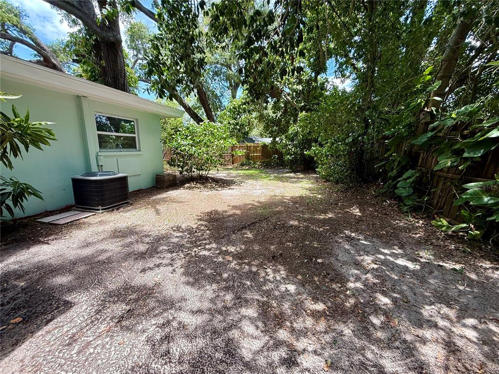 A backyard with a light green house, an air conditioning unit, and mature trees — 677 OAKWOOD DRIVE, DUNEDIN, FL