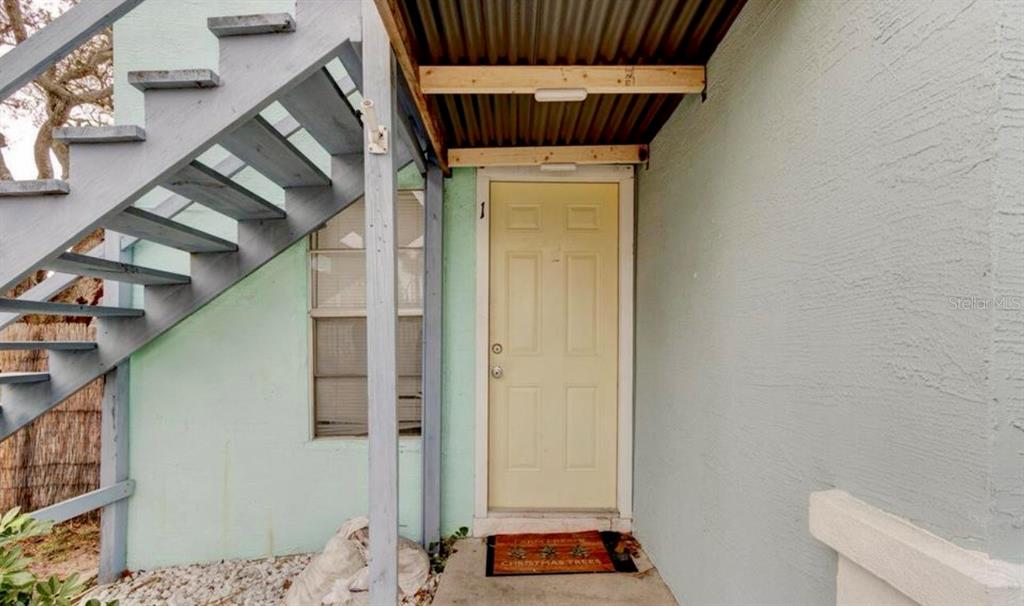 A light-colored exterior door with a number one sits beneath a metal awning and stairs — 124 S NOBLE, DAYTONA BEACH, FL