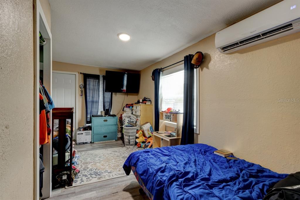 A bedroom features a blue bed, a teal dresser, a wall-mounted air conditioner, and wood-look flooring — 124 S NOBLE, DAYTONA BEACH, FL