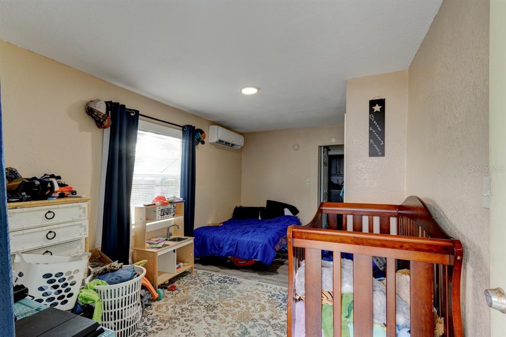 A bedroom features a crib, a bed with blue bedding, a window, and a mini-split unit — 124 S NOBLE, DAYTONA BEACH, FL
