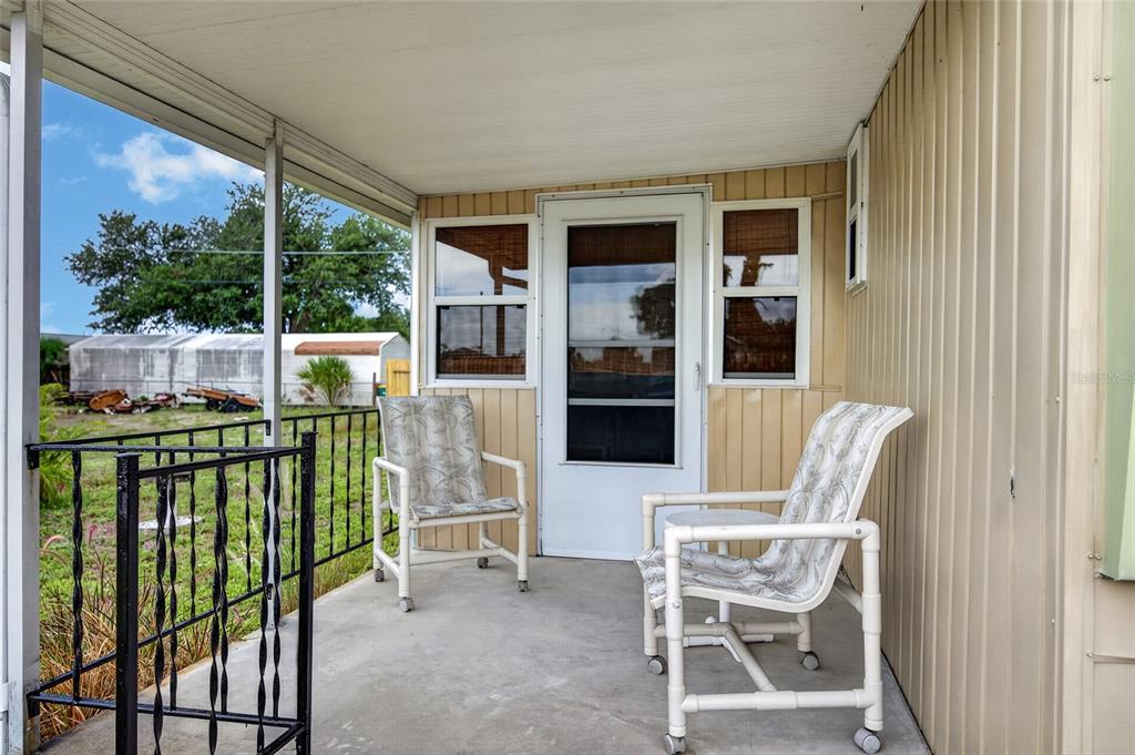 A covered concrete porch features two patio chairs, a screen door, and a black railing — 3160 10TH STREET, ENGLEWOOD, FL
