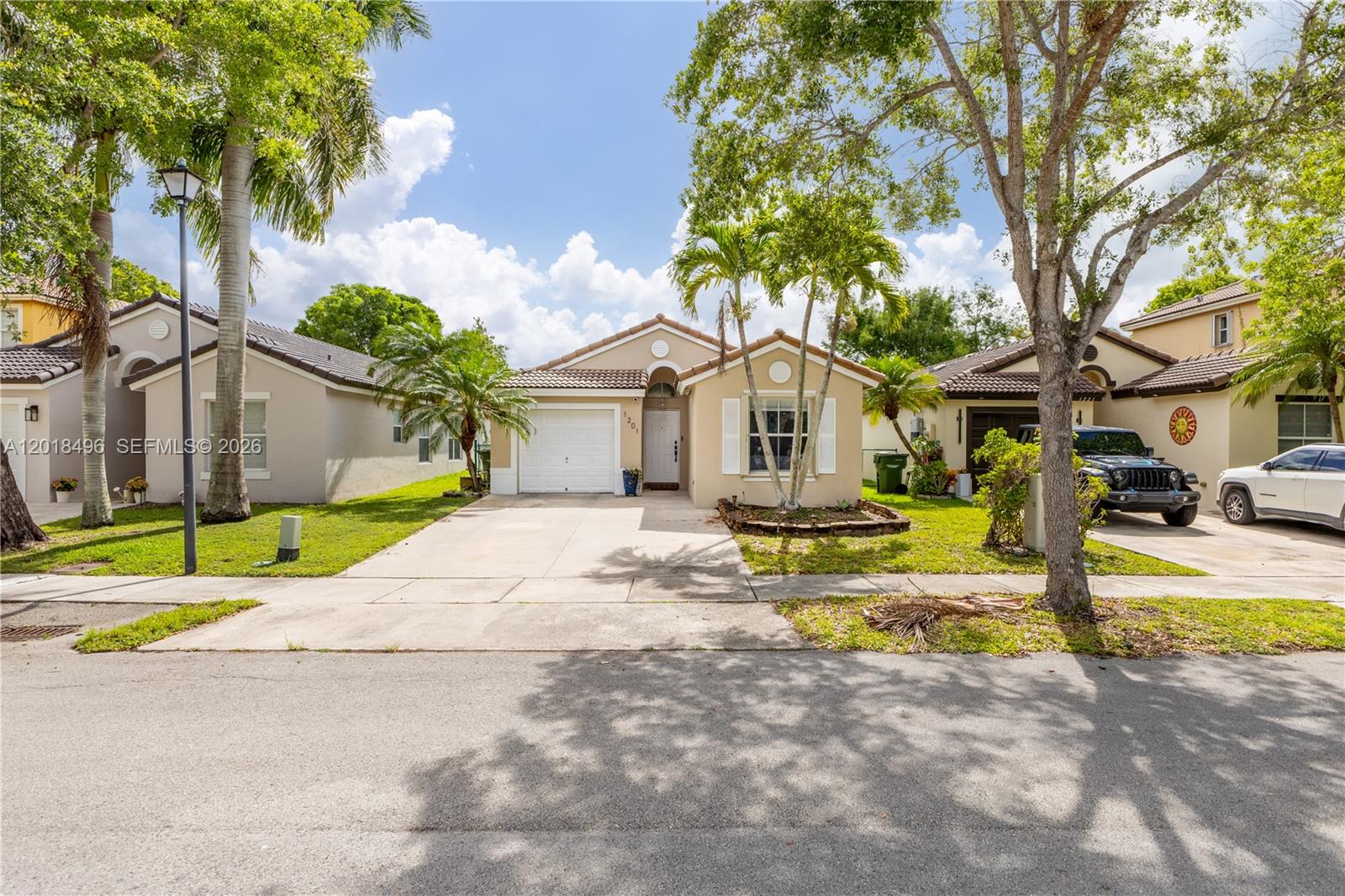 A single-story suburban house with a concrete driveway, palm trees, and a tiled roof — 1201 SE 20th Rd, Homestead FL 33035, HOMESTEAD, FL