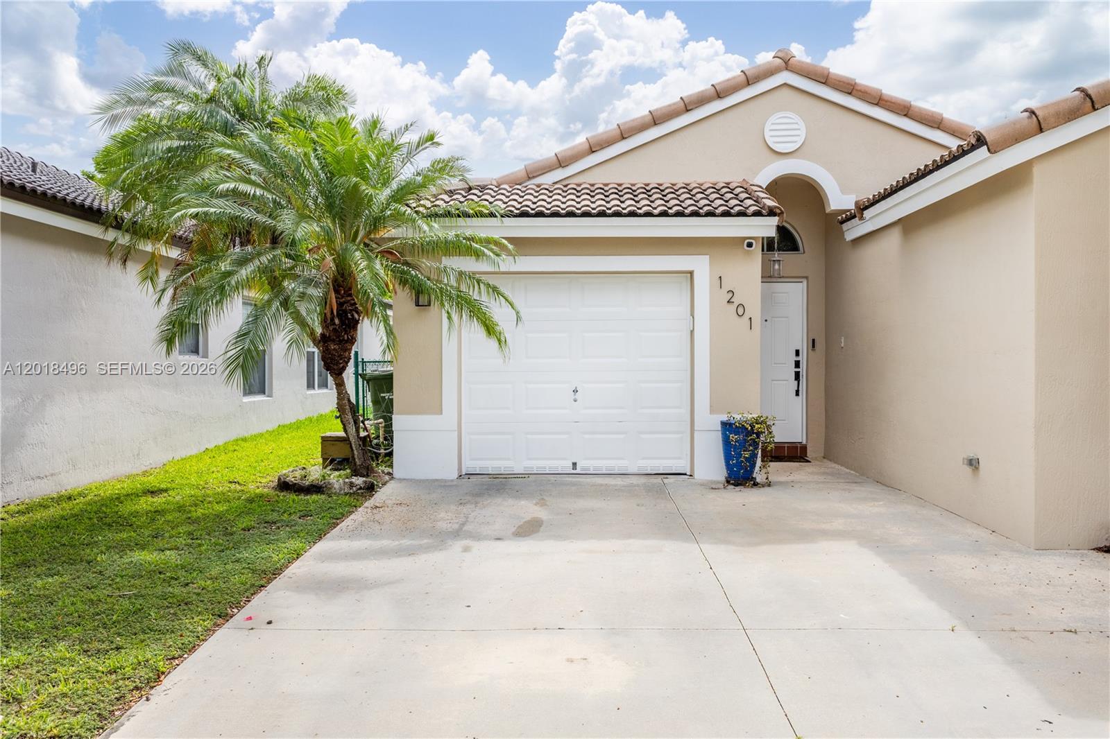 A single-story house features a white garage door, a front entrance, and a palm tree — 1201 SE 20th Rd, Homestead FL 33035, HOMESTEAD, FL