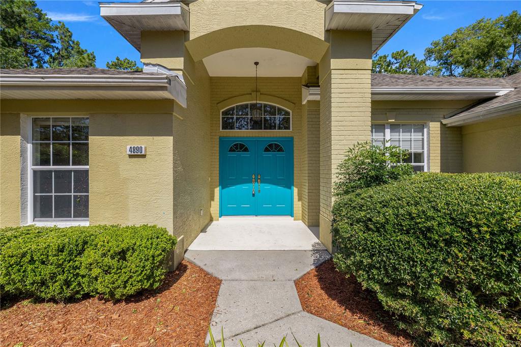 The exterior of a house features a bright blue double front door and landscaping — 4890 W GEYSER COURT, BEVERLY HILLS, FL