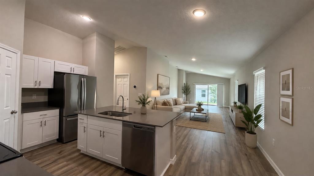 A modern kitchen with white cabinets and a quartz island opens into a living room — 4904 MAINSAIL STREET, HAINES CITY, FL