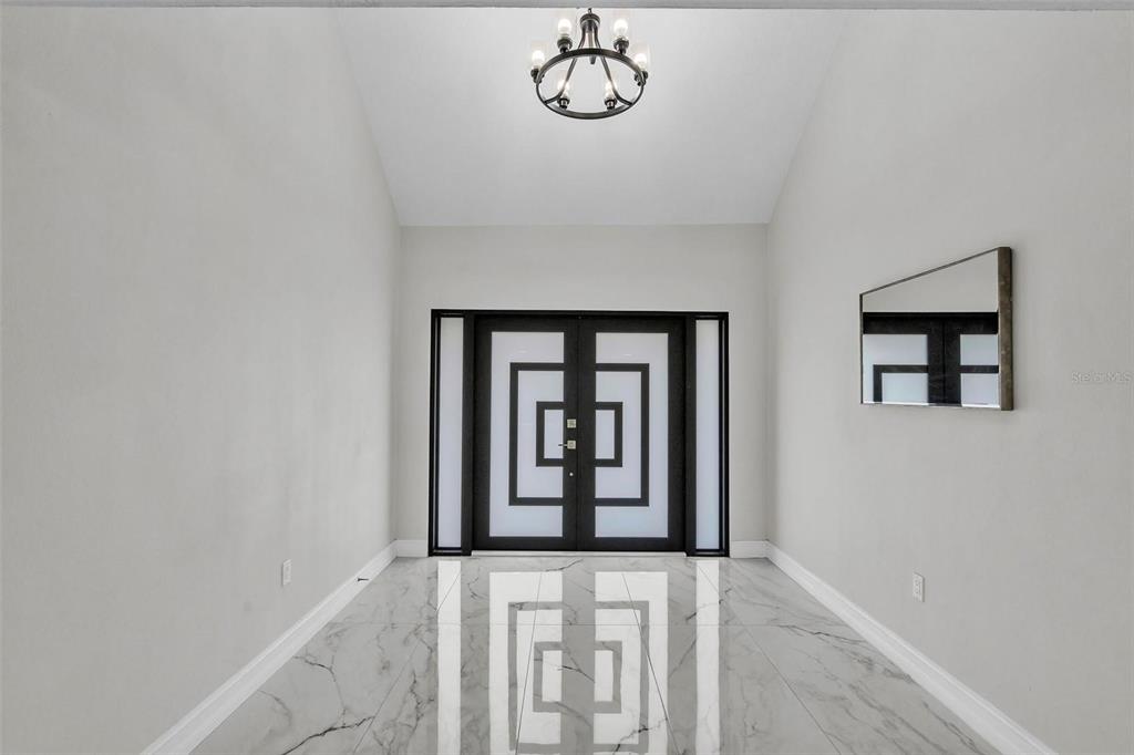 A modern entryway features a double door with geometric glass patterns and marble-look tile flooring — 4520 PINE HOLLOW DRIVE, TAMPA, FL