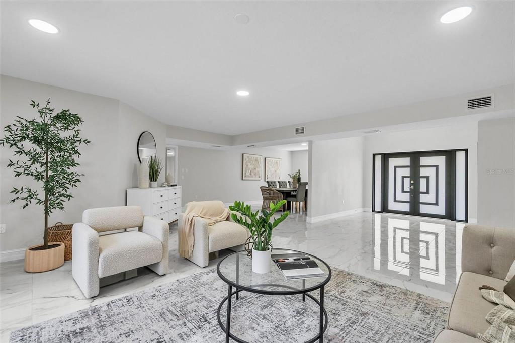 A bright, open-concept living room features white marble floors, two cream armchairs, and modern decor — 4520 PINE HOLLOW DRIVE, TAMPA, FL