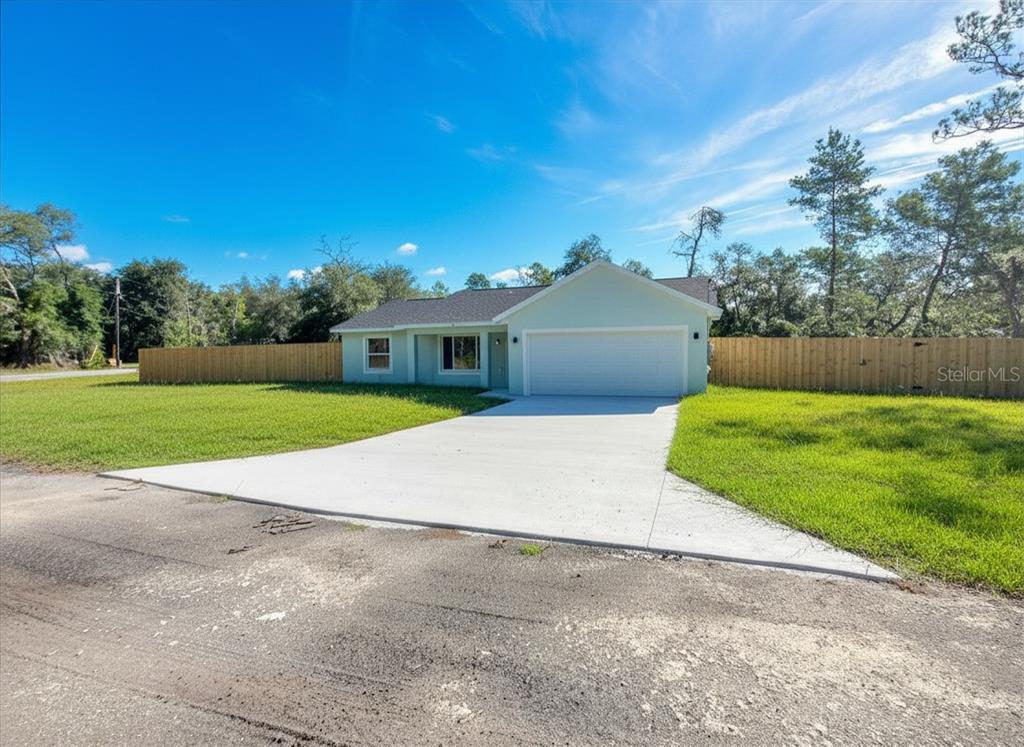 A light green single-story house with a white garage door and a wooden fence — 15 FISHER WAY PLACE, OCKLAWAHA, FL