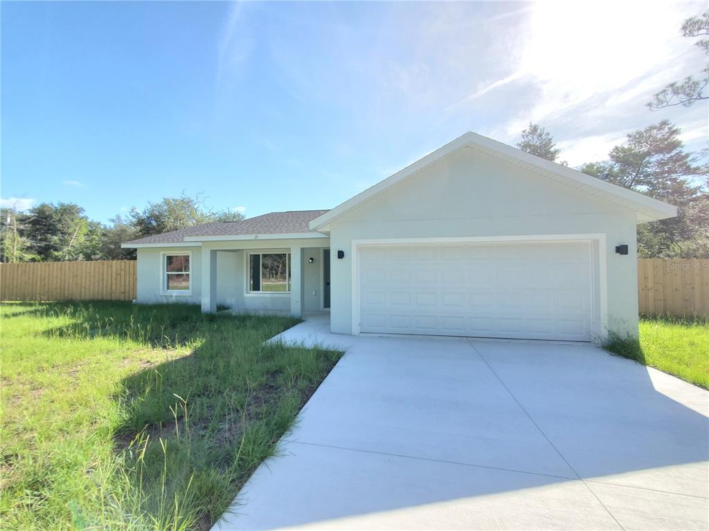 A single-story house with a white garage door, light-colored siding, and a concrete driveway — 15 FISHER WAY PLACE, OCKLAWAHA, FL