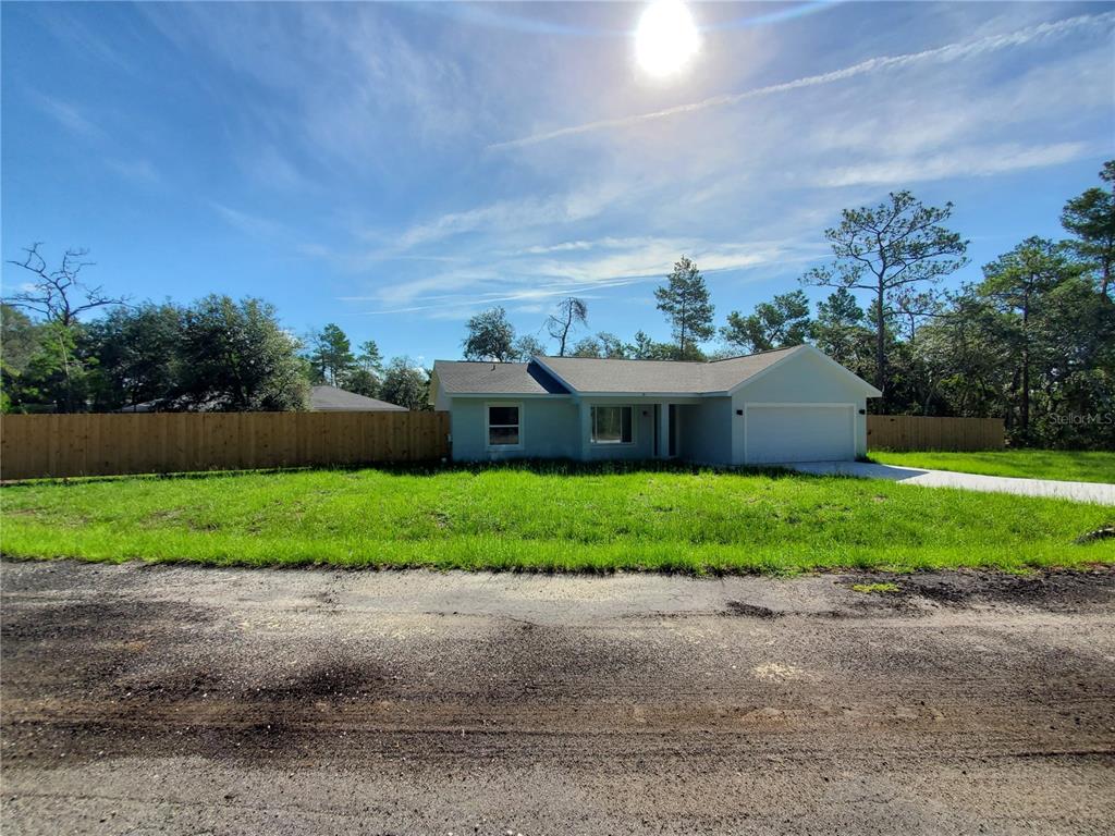 A single-story house with a garage and a wooden fence sits on a grassy lot — 15 FISHER WAY PLACE, OCKLAWAHA, FL