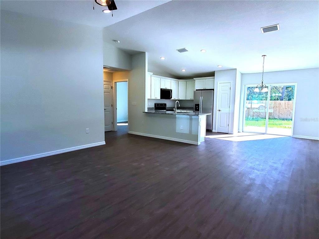 An open-concept living area features dark wood-look flooring, a kitchen with white cabinets, and sliding doors — 15 FISHER WAY PLACE, OCKLAWAHA, FL