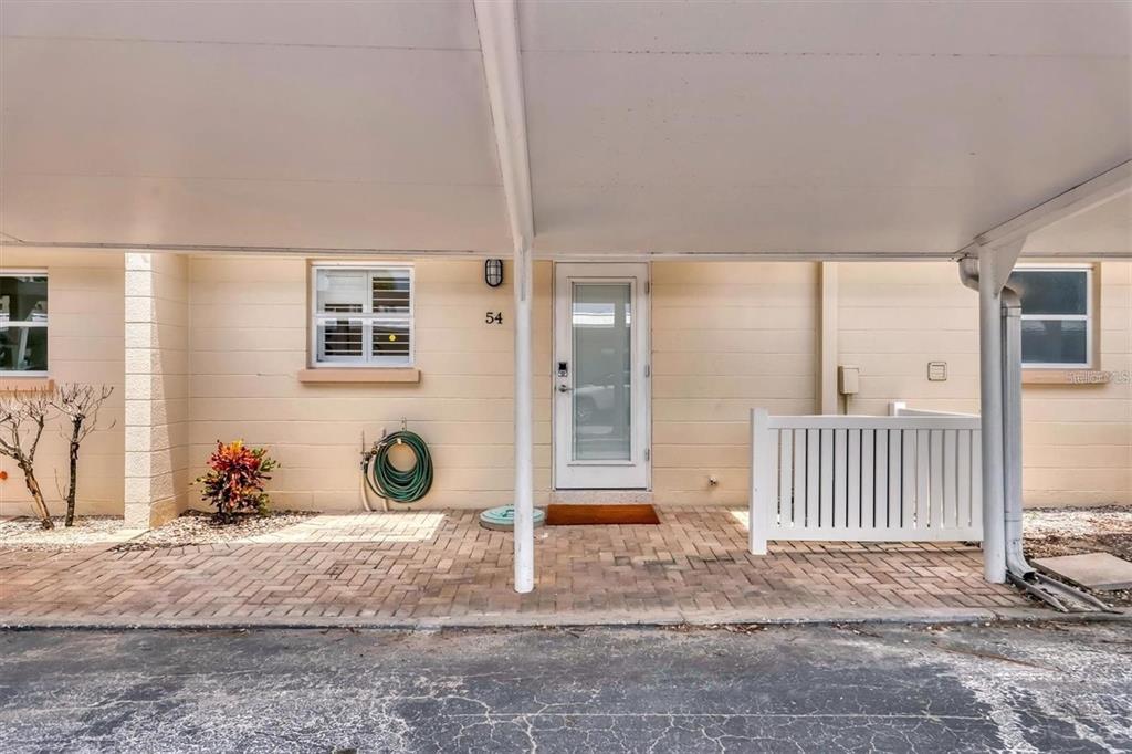 A paved patio area sits under a carport in front of a tan building entrance — 5830 MIDNIGHT PASS ROAD UNIT 54, SARASOTA, FL