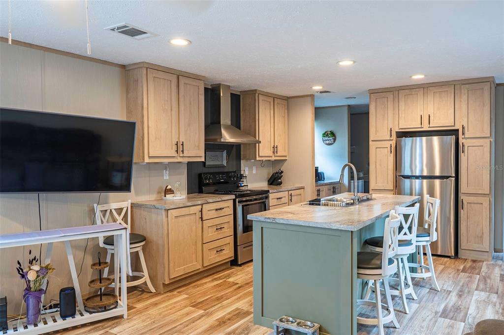 A kitchen features light wood cabinets, a green island, stainless steel appliances, and wood-look flooring — 6556 S LIMA AVENUE, HOMOSASSA, FL