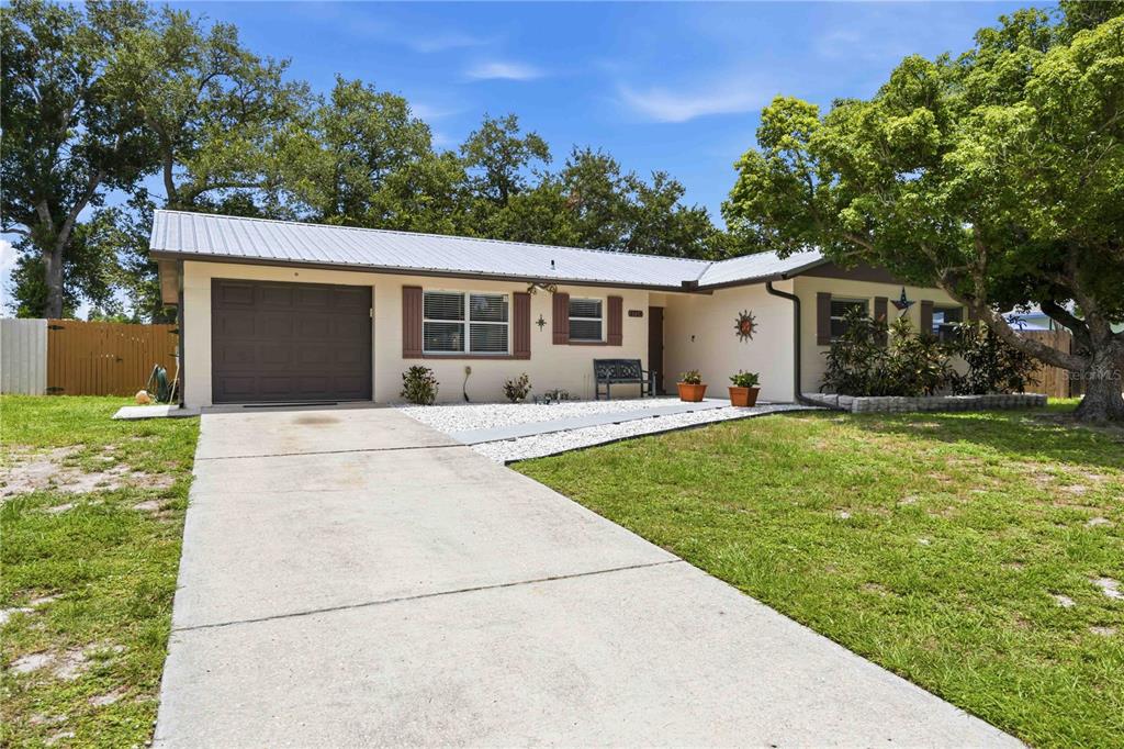 A single-story house with a metal roof, beige siding, and a concrete driveway — 3718 WOODMONT DRIVE, SARASOTA, FL
