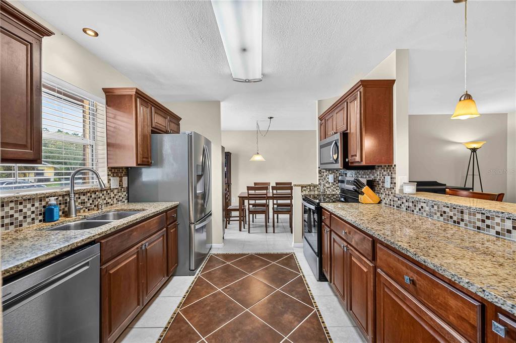 A kitchen with wood cabinets, granite countertops, stainless steel appliances, and a tiled floor — 3718 WOODMONT DRIVE, SARASOTA, FL