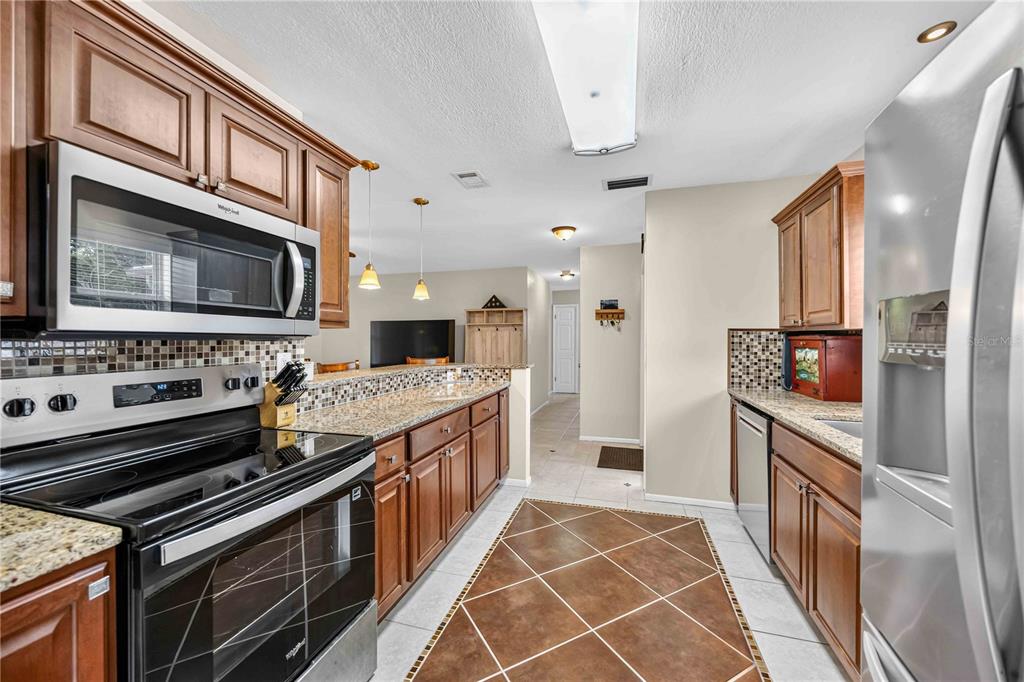 A kitchen features wood cabinets, stainless steel appliances, granite countertops, and a tiled floor — 3718 WOODMONT DRIVE, SARASOTA, FL