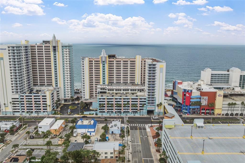 An aerial view shows high-rise beachfront hotels and parking structures near a coastal road — 300 N ATLANTIC AVENUE UNIT 405, DAYTONA BEACH, FL