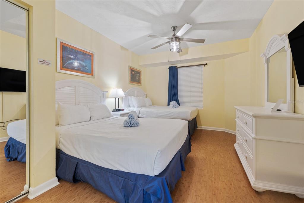 A bedroom features two beds with white linens, blue bed skirts, and light wood flooring — 300 N ATLANTIC AVENUE UNIT 405, DAYTONA BEACH, FL