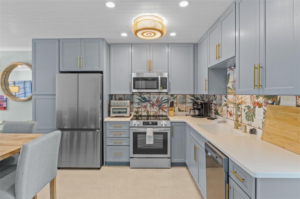 A kitchen features light blue cabinets, stainless steel appliances, and a tropical-patterned tile backsplash — 26 SEASIDE COURT, HOLMES BEACH, FL