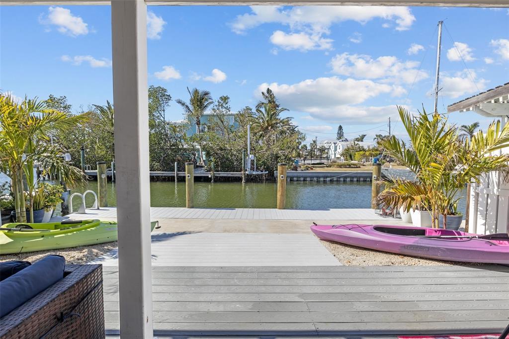 A wooden deck overlooks a canal with two kayaks and a boat dock — 26 SEASIDE COURT, HOLMES BEACH, FL