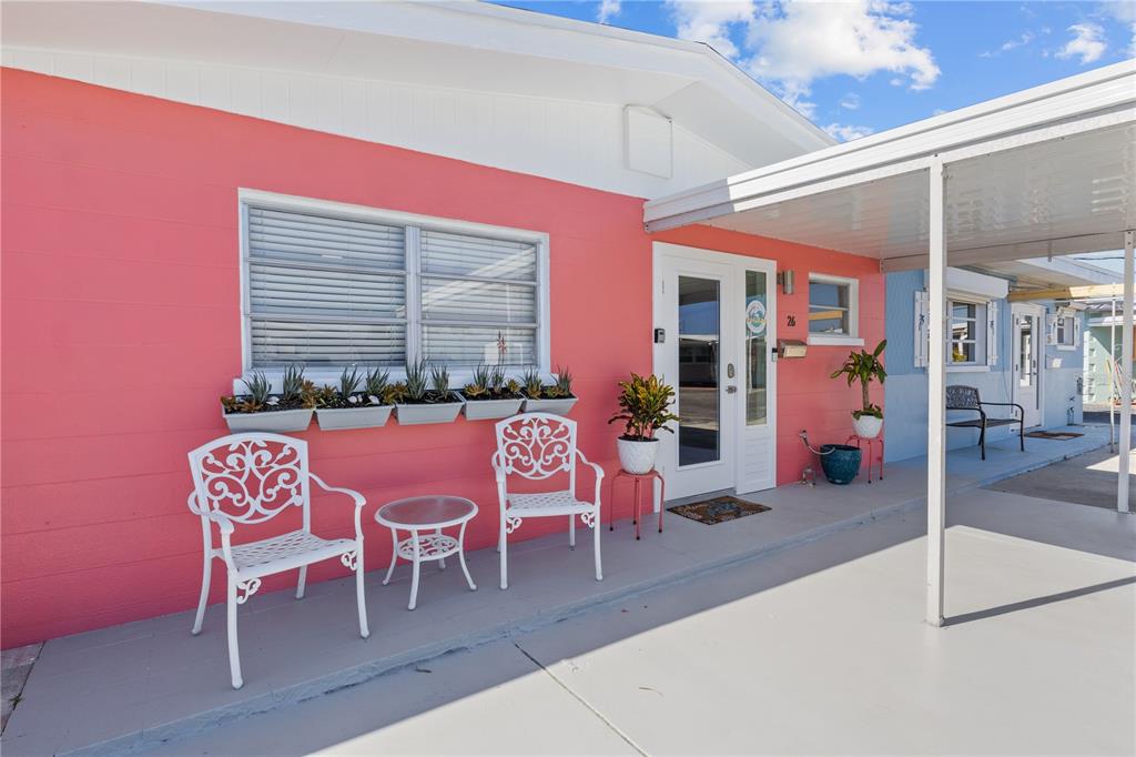 A pink exterior wall features a window with planters, two white chairs, and a carport — 26 SEASIDE COURT, HOLMES BEACH, FL