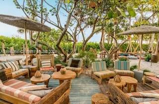An outdoor lounge area features wooden furniture, striped cushions, and umbrellas under a canopy of trees — 102 24th St # 1421, Miami Beach FL 33139, MIAMI BEACH, FL