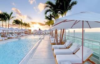 A rooftop swimming pool lined with lounge chairs and umbrellas overlooking the ocean at sunset — 102 24th St # 1421, Miami Beach FL 33139, MIAMI BEACH, FL
