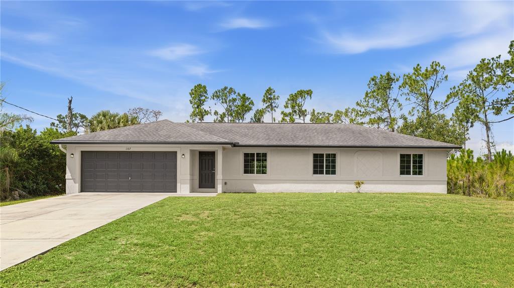 A single-story house with a gray garage door, white exterior, and a large front lawn — 1167 URMEY LANE, NORTH PORT, FL