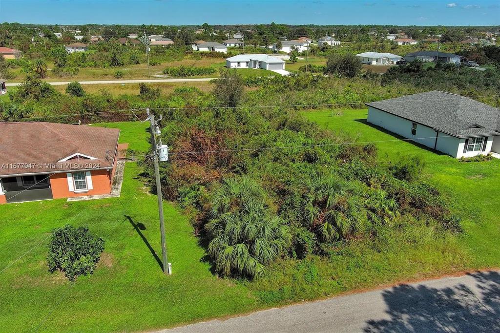 An aerial view shows a vacant, overgrown lot situated between two single-family homes — 2912 61ST STREET W, LEHIGH ACRES, FL