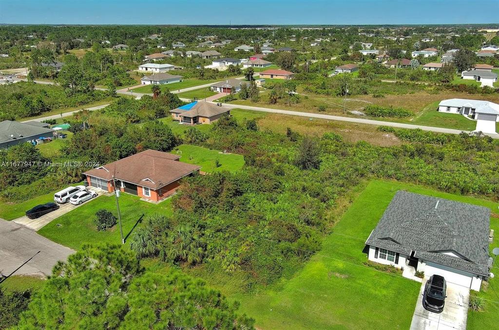An aerial view shows two houses separated by a large, undeveloped, brush-covered lot — 2912 61ST STREET W, LEHIGH ACRES, FL