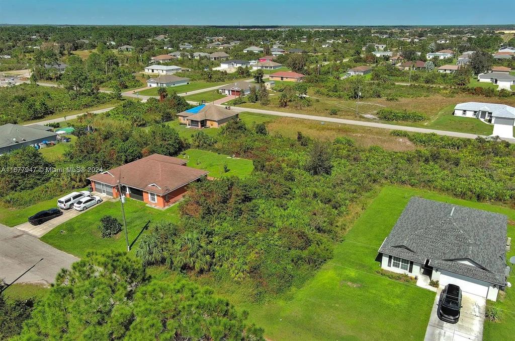 An aerial view shows two houses separated by a large, undeveloped, brush-covered lot — 2912 61ST STREET W, LEHIGH ACRES, FL