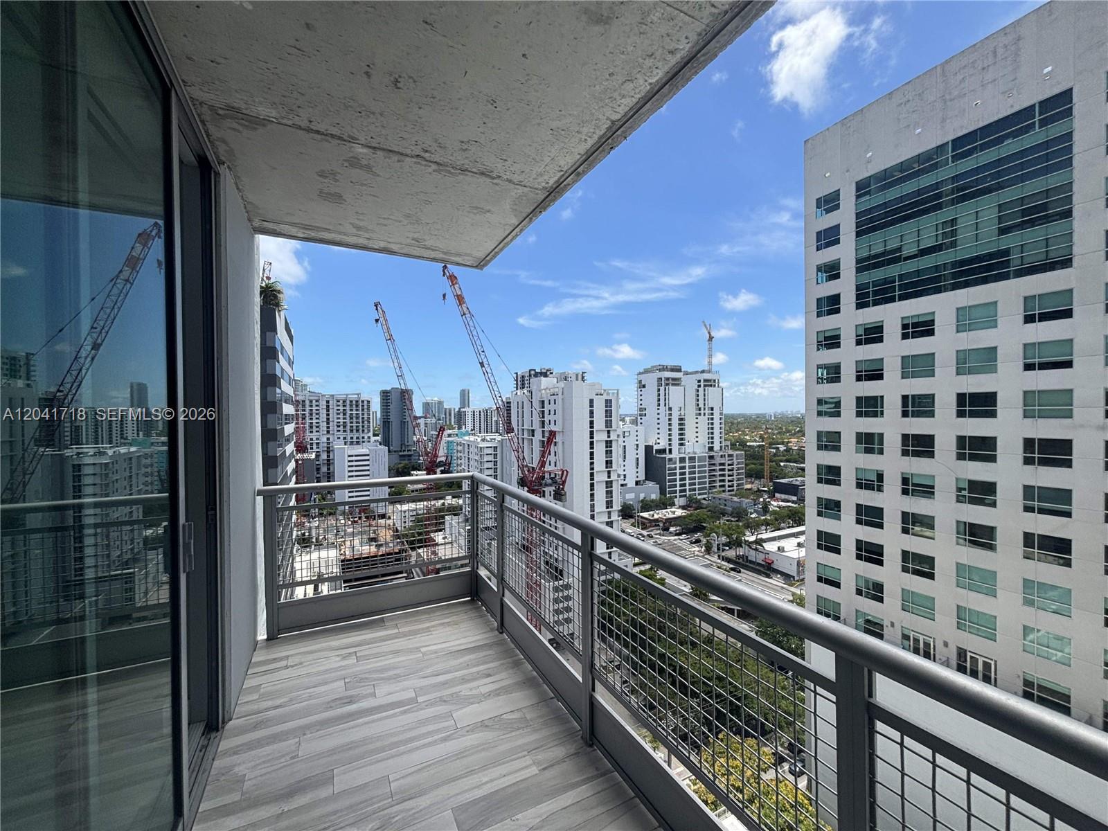 A balcony with wood-look tile flooring overlooks a city skyline featuring several construction cranes — 690 SW 1st Ct # 2124, Miami FL 33130, MIAMI, FL