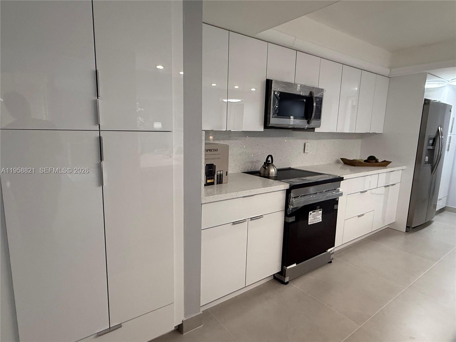 A modern kitchen features white high-gloss cabinets, stainless steel appliances, and light-colored countertops — 950 Egret Cir # 5409, Delray Beach FL 33444, DELRAY BEACH, FL
