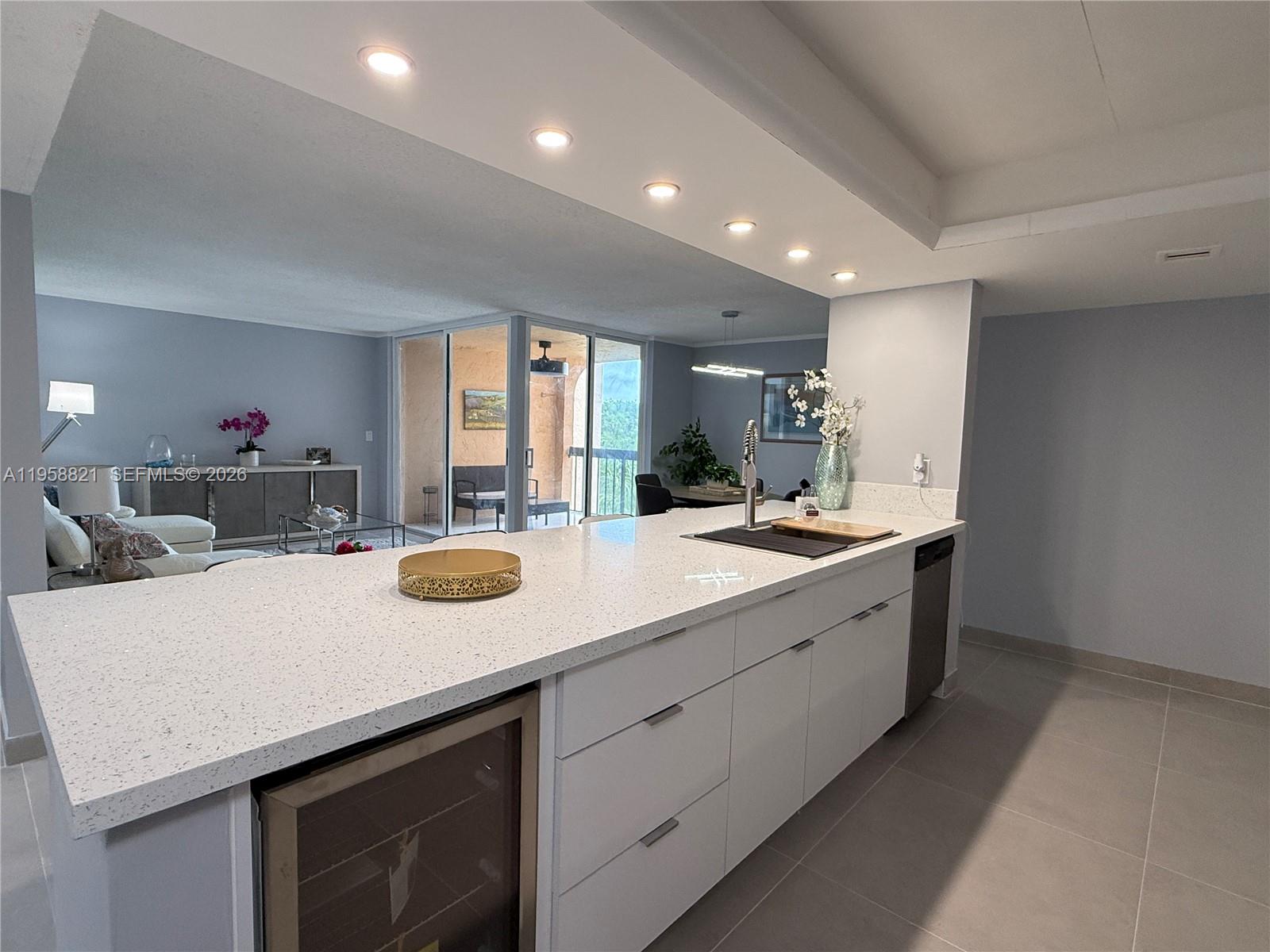 A modern kitchen island with white quartz countertops and cabinetry overlooks an open living area — 950 Egret Cir # 5409, Delray Beach FL 33444, DELRAY BEACH, FL